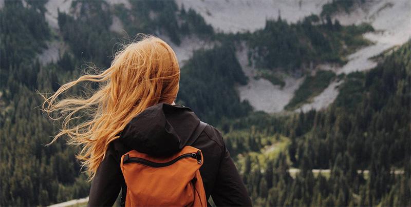 back of female head with backpack, mountains in backdrop