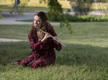 student playing flute seated on grass